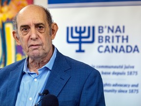 A man in a blue suit is standing towards the left of the frame, to the right there's a sign reading B'nai Brith Canada.