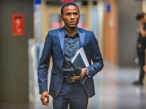 Mamadi Fara Camara walks down a courthouse corridor wearing a suit and holding documents