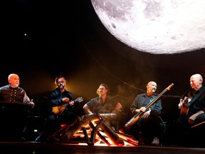 Peter Gabriel at left with band members under a screen showing a huge full moon.