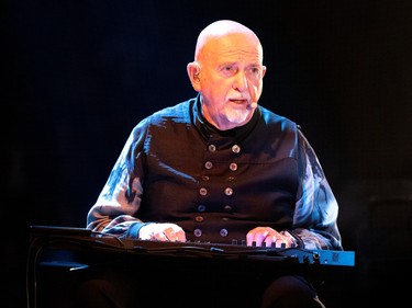 Closeup of Peter Gabriel performing at a keyboard. He's wearing a dark shirt with two rows of buttons.