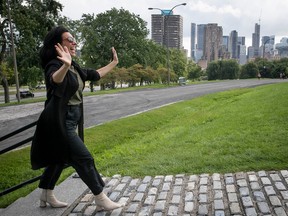 Montreal Mayor Valérie Plante gestures with open arms in front of a green space with the city's skyline in the background.