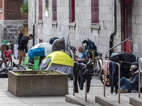 Tents, bikes and bags of belongings are set up outside a building with a red door and barred windows.