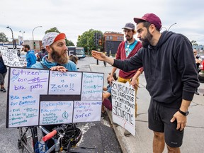 Two men argue on a street. One of them holds signs in favour of bike paths.