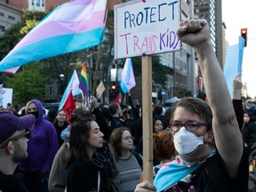 A man in a mask holds a sign reading "Protect trans kids" amid a crowd of protesters.