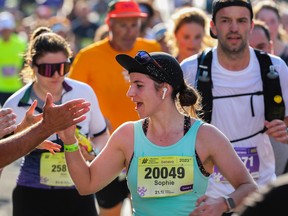 A runner in a green tank top gives a high five during a marathon. There are runners behind her.