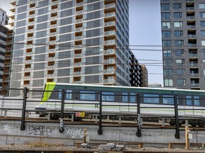 An electric train is passing over a rail line backdropped by residential buildings.