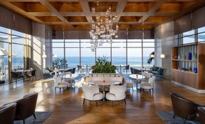 A lobby with a modern chandelier and white chairs and tables overlooking the Mediterranean Sea.