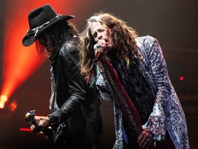 Joe Perry plays a guitar while Steven Tyler sings into a microphone during a show