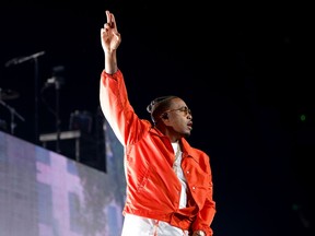 A man is wearing a red/orange jacket onstage with his hand in the air while performing.