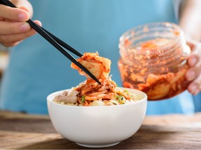 A person serves kimchi with chopsticks from a glass jar.