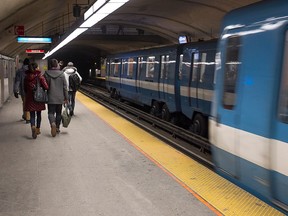 People are walking along a metro platform on the left side of the frame while trains arrive at the station to the right.