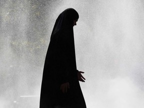 A woman wearing a hijab walks through a water spray