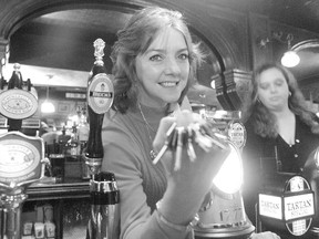 A black and white photo shows Teresa Slevin holding a set of keys posing for a photo behind the bar