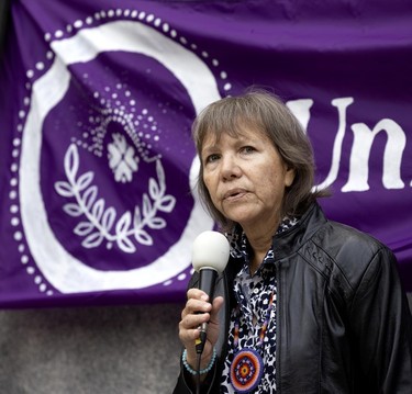 Indigenous rights advocate Ellen Gabriel speaks into a microphone in front of a purple banner draped by a monument.