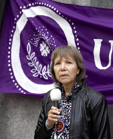 Indigenous rights advocate Ellen Gabriel speaks into a microphone in front of a purple banner draped by a monument.