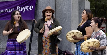 Four women play traditional drums in front of a banner placed by a monument.