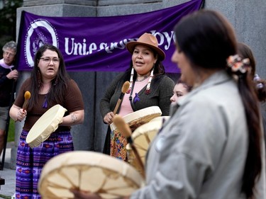 A group of women play traditional drums in front of a banner placed by a monument.
