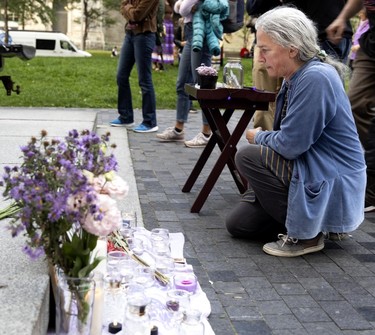 A woman kneels on a paved surface in front of a memorial made up of candles and flowers.