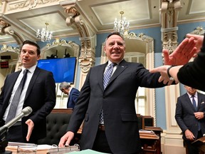 Francois Legault extends his hand to an unseen person in the Blue Room of Quebec's National Assembly. Simon Jolin-Barrette is beside him.