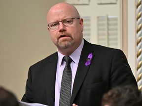 Ian Lafrenière stands in the National Assembly wearing a purple ribbon