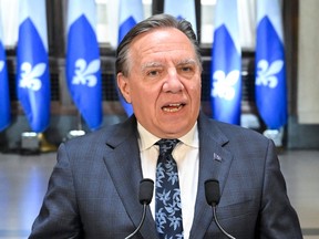 François Legault speaks at a microphone in front of Quebec flags