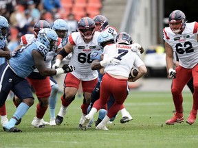 Argonauts defenders, in double blue, swarm Alouettes quarterback Cody Fajardo, in white, with red pants, for a sack.