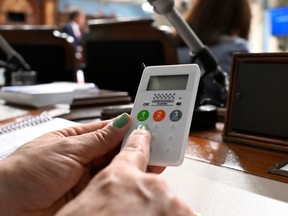 An electronic device with a number pad and National Assembly logo is held over a desk at the legislature