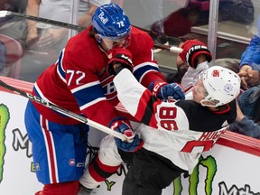 Canadiens defenceman Arber Xhekaj, in the Habs classic red home jersey, checks Devils' Jack Hughes into the boards.