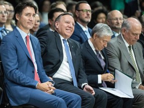 Justin Trudeau and François Legault sit next to each other in a crowd