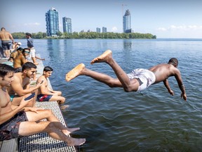 Ousmane Traore dives off a dock into the St. Lawrence River with others sitting on the dock and a skyline in the background