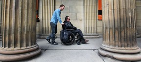 Playwright David Fennario is pushed in a wheelchair in front of pillars outside Centaur Theatre.