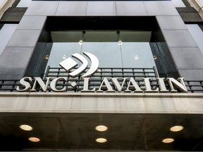 A sign on a building reading SNC-Lavalin in gold letters is seen at the centre of the image, surrounded by stone siding. The sign is in front of a window.