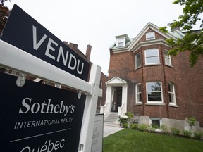 A "vendu" sign is taking up the left side of the frame while the right side features a two-storey brick house and a bit of a front lawn consisting of grass.