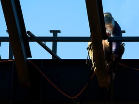 A welder works on large beams with a blue sky in the background.