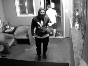 Black-and-white surveillance camera image of a man in an Adidas hoodie walking into a motel lobby