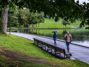 Two people, one with an umbrella, walk on the path beside Beaver Lake on a cloudy day.