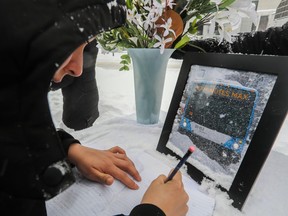 a woman with a hood on is signing a book in front of a photo of a bus.