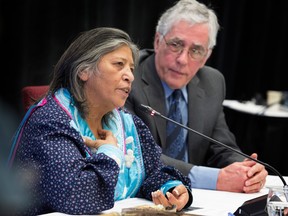 Sedalia Kawennotas speaks into a microphone at a table while Jacques Viens listens