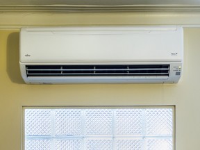 A heat pump is on a yellow wall above a window.