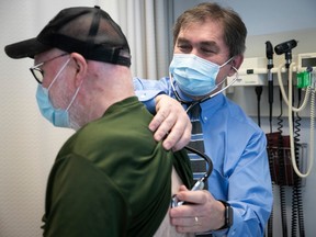 A masked doctor listens to the heart of a senior patient.