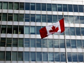 A Canadian flag on a pole in front of office building windows