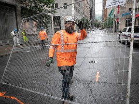 A construction worker wearing safety orange and a hard hat removes a large piece of steel fencing from a street.