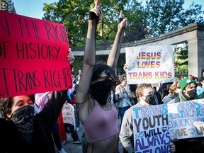 Demonstrators hold protest signs that read "Jesus loves trans kids" and "trans youth will always belong."