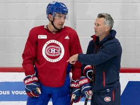 Canadiens head coach Martin St. Louis, wearing a dark blue jacket and skates, stands next to captain Nick Suzuki on the ice during training camp last month.