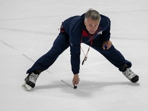 Canadiens head coach Martin St. Louis seen bending over on his skates with a marker in his right hand as he draws a line on the ice during practice.