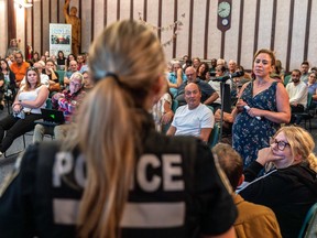 A woman wearing a police uniform is seen from behind facing a crowd of residents at a town hall meeting