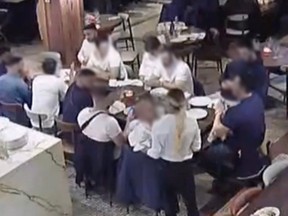 Several people are seeing from surveillance footage sitting at a table at a restaurants, most of them with blurred faces due to a publication ban.