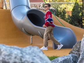 A young boy in a Canadiens #12 jersey and sunglasses walks along an orange surface next to a playground slide