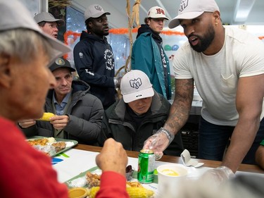 The Montreal Alouettes' Darnell Sankey, wearing a T-shirt and cap, talks to a man as the player serves Thanksgiving dinner at the Welcome Hall Mission.