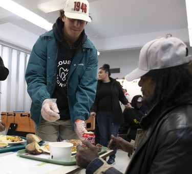 The Montreal Alouettes' Greg Ellingson, wearing a team shirt and jacket, gives a tray of Thanksgiving dinner to a man at the Welcome Hall Mission.